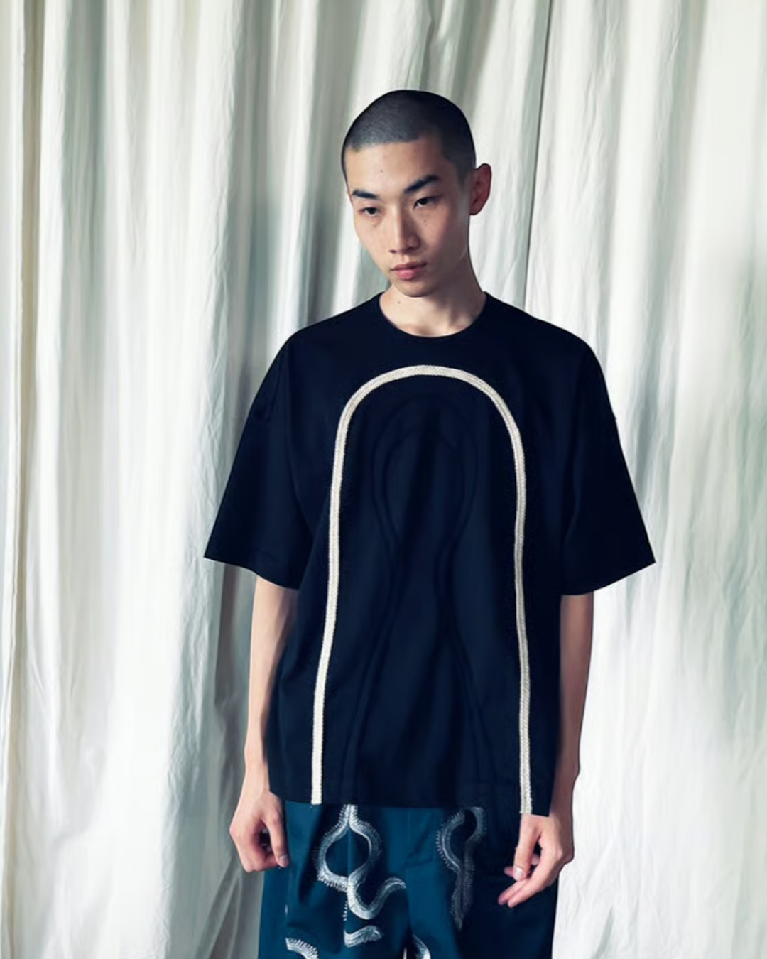 CALCÈLの黒い綿100%天竺Tシャツ。フロントにコード糸でお地蔵さんのシルエットが描かれたゆったりとしたデザイン。