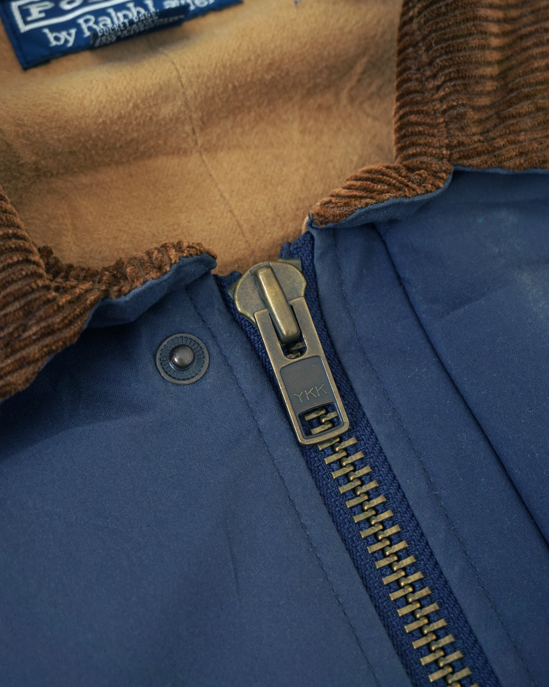CALCÈLで取り扱うPolo by Ralph Laurenのヴィンテージユーティリティジャケット。茶色のコーデュロイ襟と青いコットン生地、YKKジッパーが特徴。