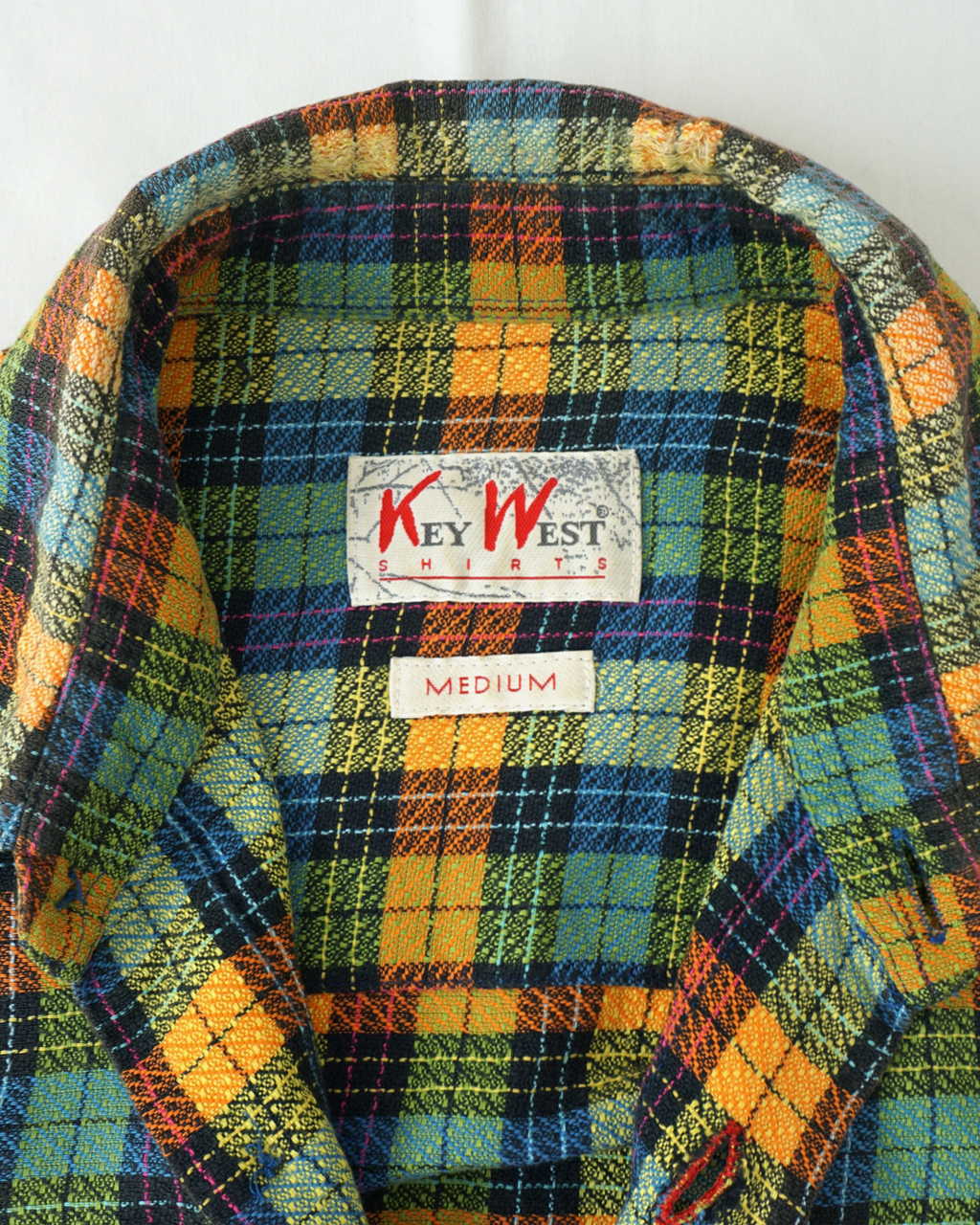 CALCÈLのKey West Shirts製、オレンジや青など多色使いのチェック柄長袖シャツ。襟元のブランドタグとサイズタグのクローズアップ。