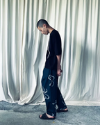 CALCÈLの黒いTシャツを着用し、お地蔵さんの刺繍が施されたパンツを合わせた男性モデルの全身ショット