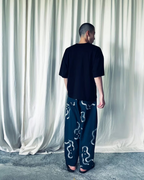 CALCÈLのohta黒色コットンTシャツを着用し、お地蔵さんのシルエット柄パンツを合わせた男性の背面ショット