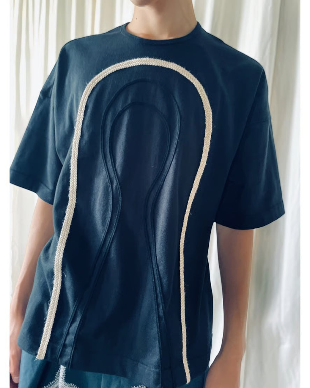 CALCÈLの黒い綿100%天竺Tシャツ。フロントに2種類のコード糸でお地蔵さんのシルエットがデザインされたゆったりとしたシルエットのアイテム。