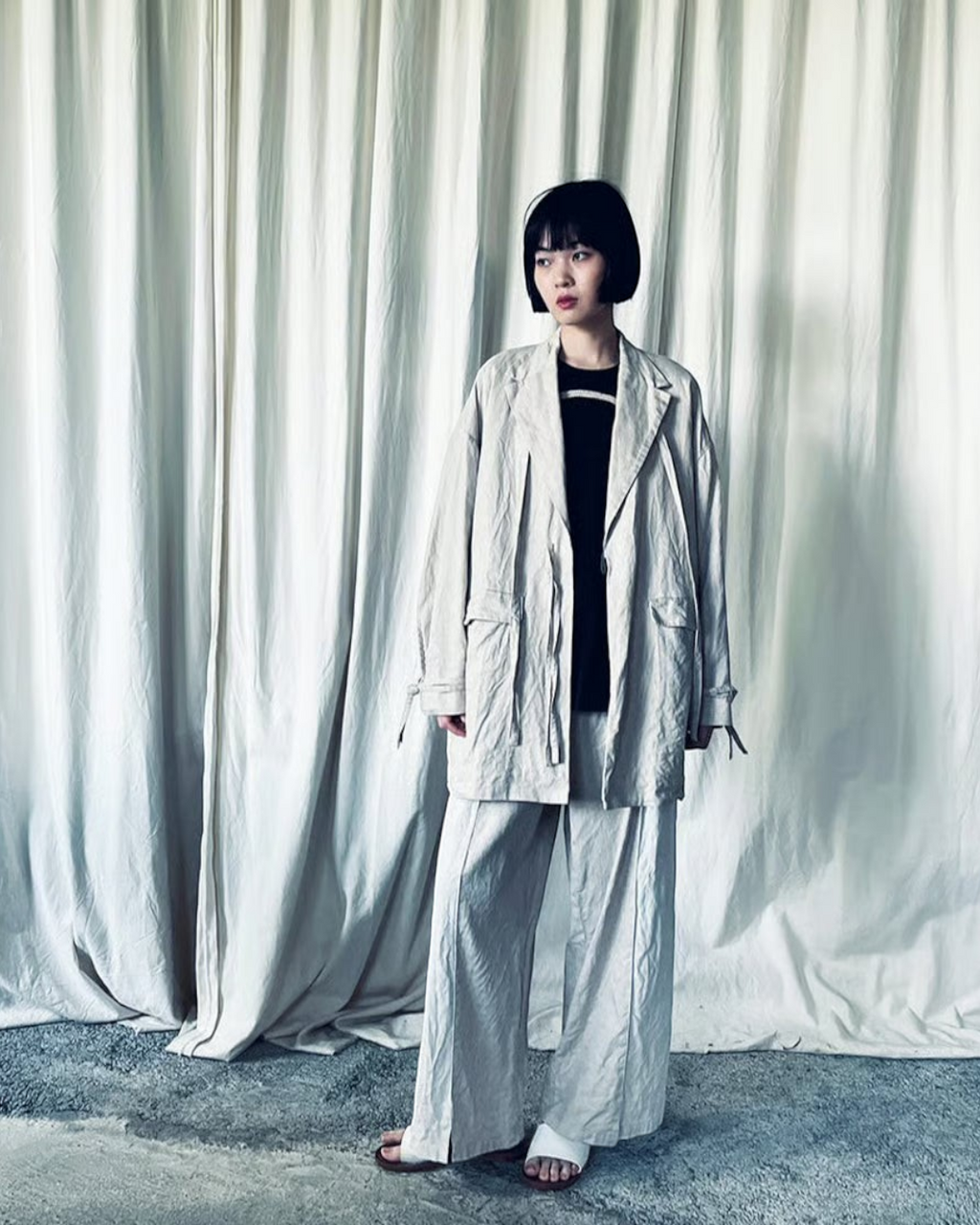 CALCÈLのohta黒い地蔵Tシャツを着用し、ベージュのセットアップを羽織ったショートボブの女性モデル