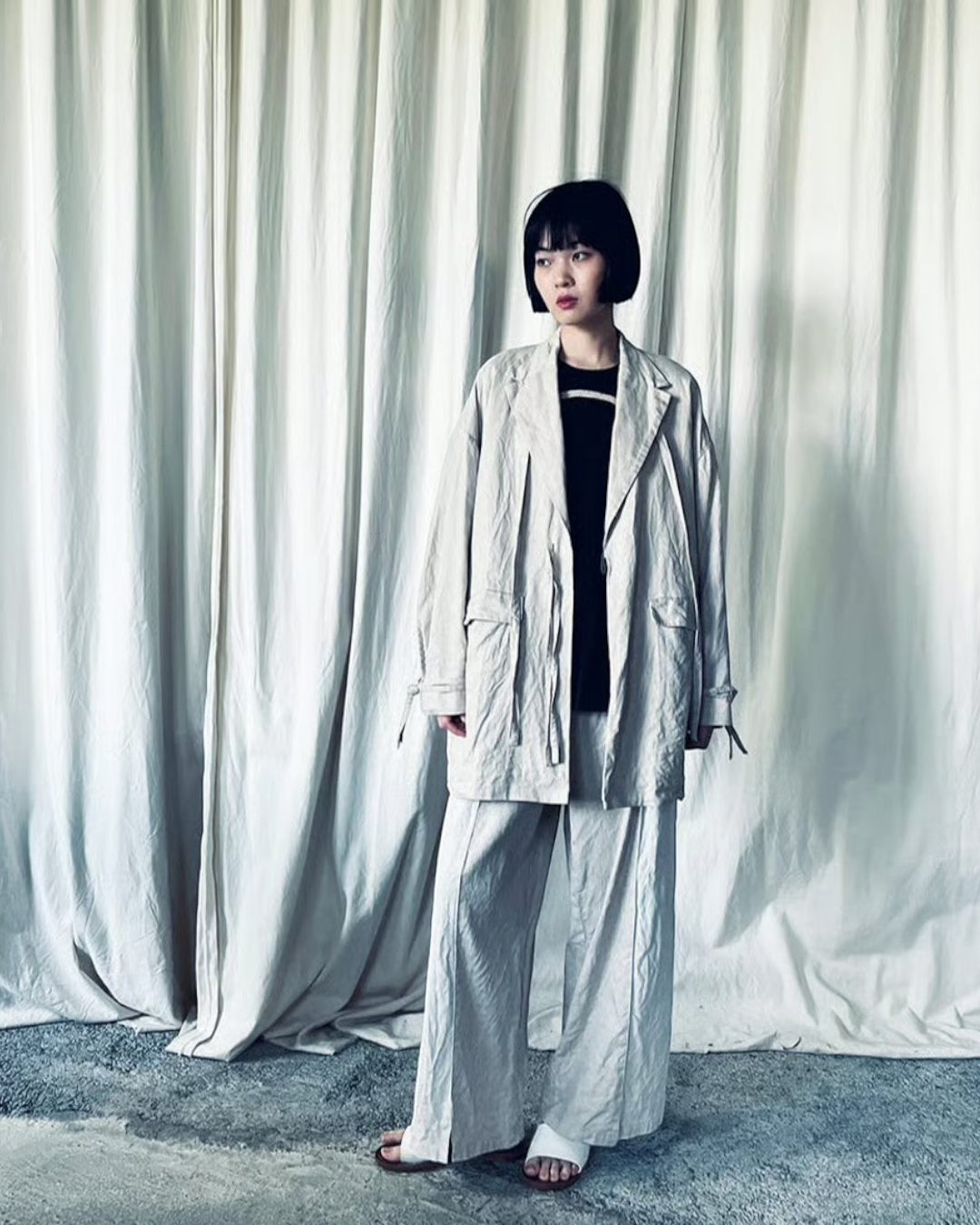 CALCÈLのohta黒い地蔵Tシャツを着用し、ベージュのセットアップを羽織ったショートボブの女性モデル